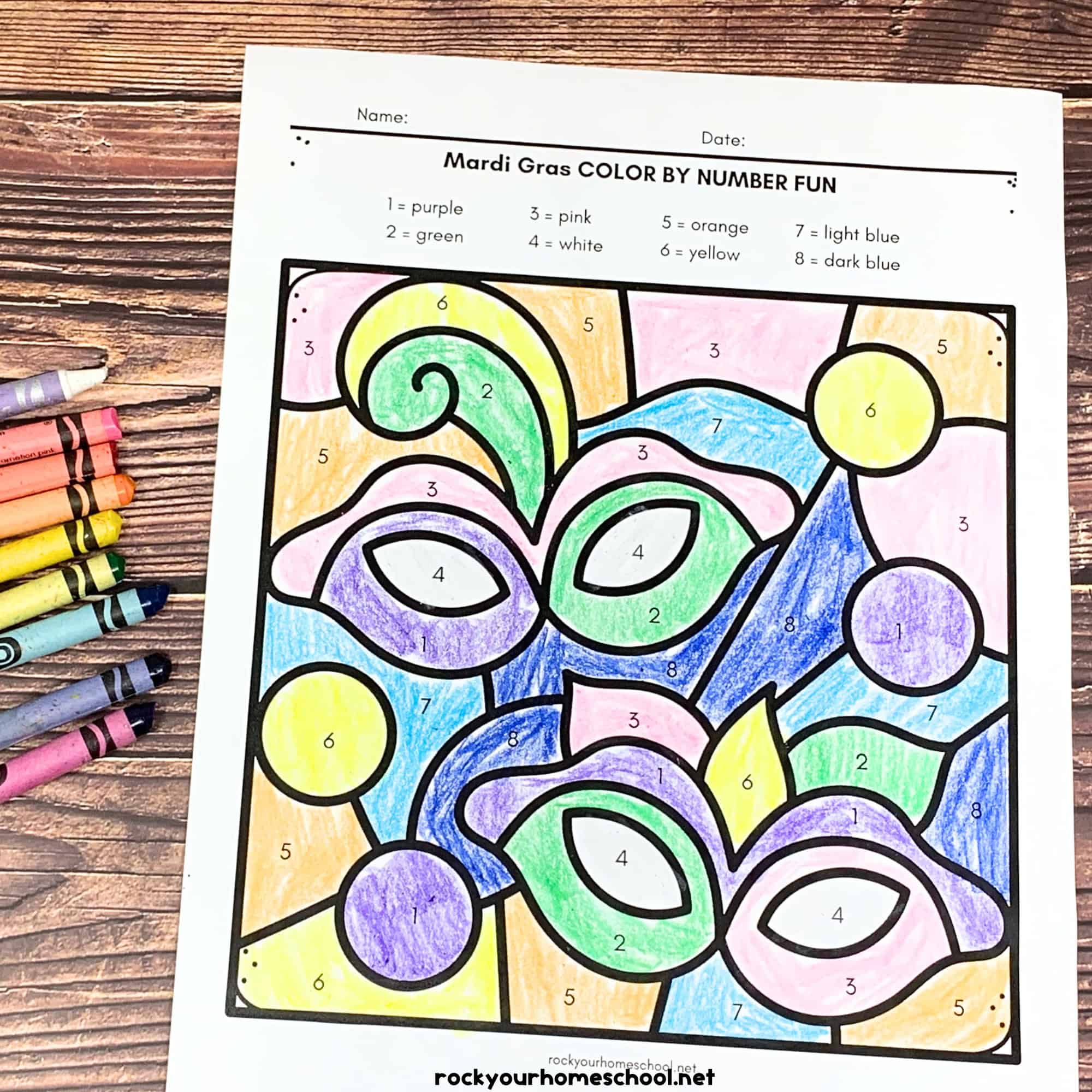 A completed Mardi Gras color-by-number page with colorful masks, beads, and numbered sections, alongside crayons on a wooden surface.