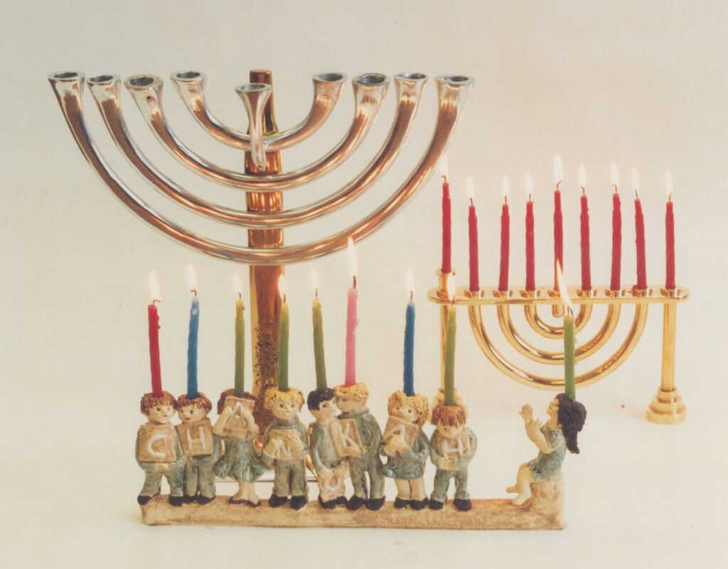 A large brass menorah and a smaller candleholder stand behind a row of small figurines holding colorful candles.